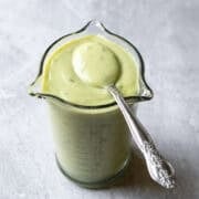 Avocado lime ranch dressing in a small glass jar with a spoon dipped to show creamy consistency.