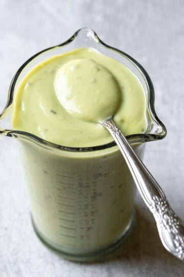 Avocado lime ranch dressing in a small glass jar with a spoon dipped to show creamy consistency.