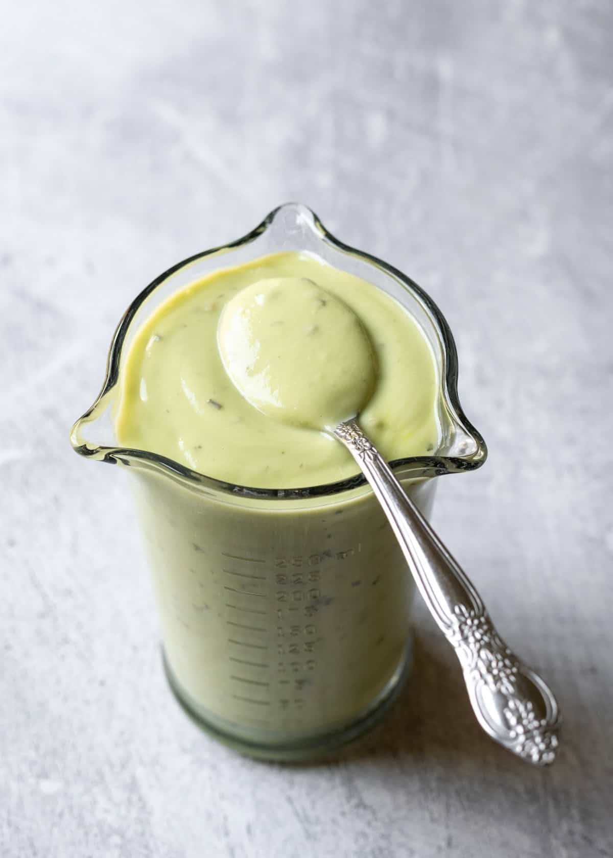 A glass jar filled with homemade avocado ranch dressing and a spoonful resting on top.