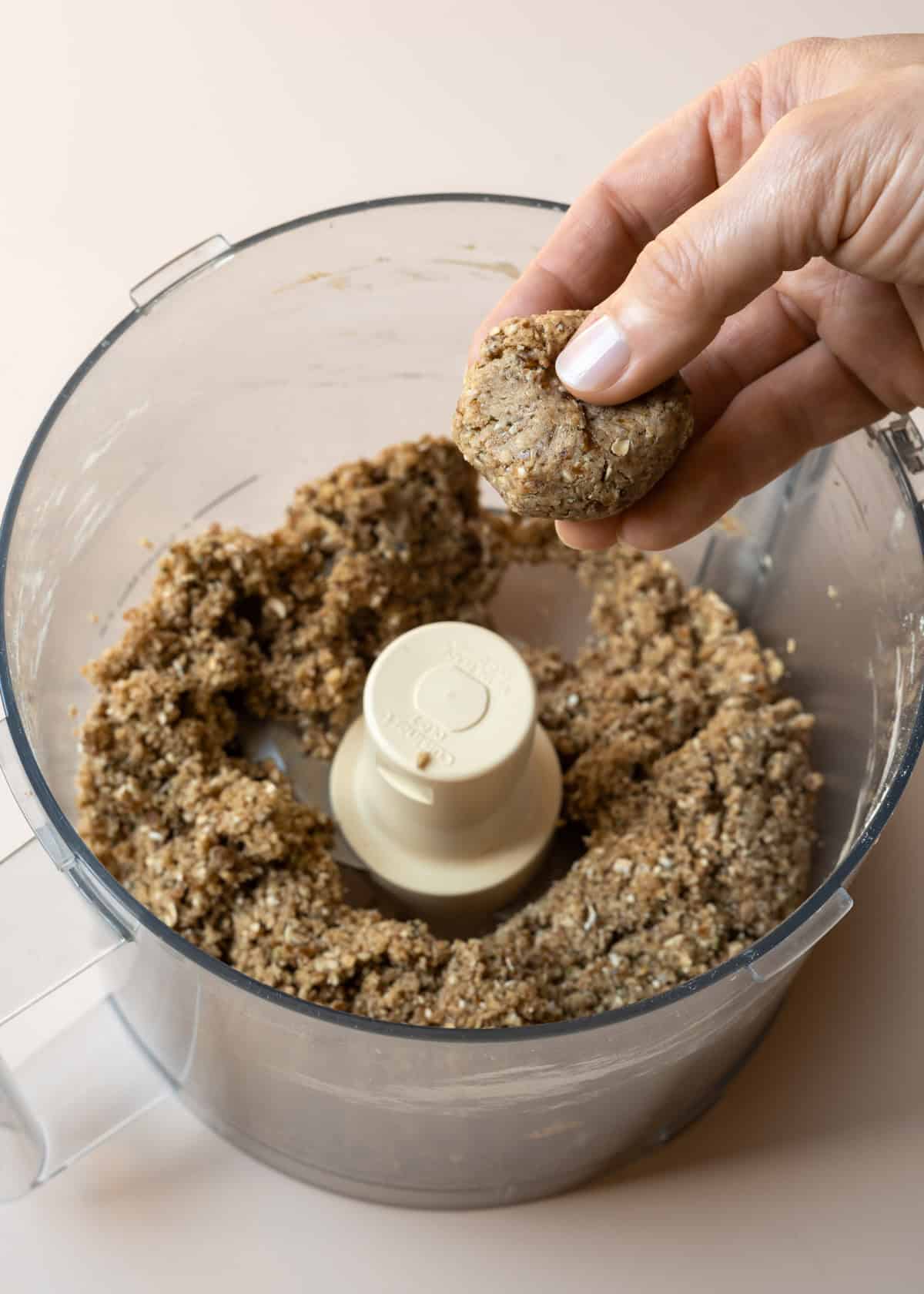 The blended protein ball mixture in a food processor with a hand showing how it holds together.