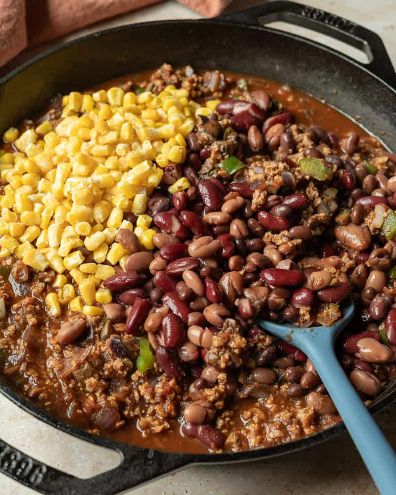 Adding beans and corn to the pot of chili.