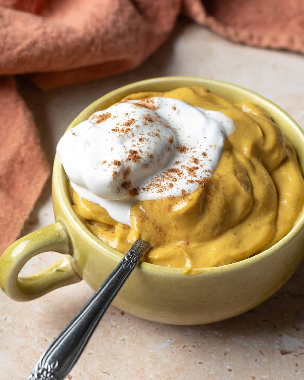 A small cup filled with creamy pumpkin mousse topped with non-dairy whipped cream.