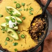 Vegan chili cornbread casserole in a cast iron skillet topped with avocado and cilantro.