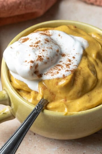 A small tea cup filled with vegan pumpkin mousse topped with non-dairy whipped cream.